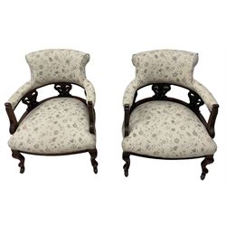 Pair late Victorian mahogany framed tub armchairs, scrolled back over pierced and carved foliate splats, sprung seat upholstered in ivory ground floral fabric, on cabriole supports with castors