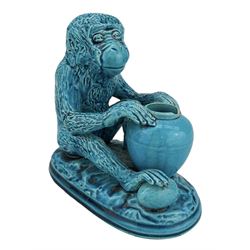 Burmantofts Faience turquoise-glaze model of a monkey, modelled seated resting on a vase, his foot resting on a large nut, on fluted oblong base, impressed factory marks beneath, model no. 782, H15cm x L16cm