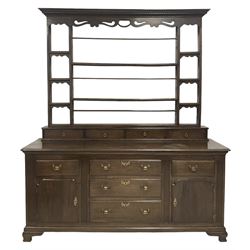 George III oak dresser, the projecting dentil cornice and shaped and pierced apron over two plate racks, six small shelves and four spice racks, leading to base with five drawers and two cupboards, raised on ogee bracket supports 