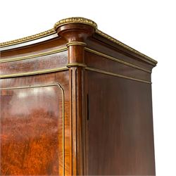 Mid-to-late 20th century parcel gilt walnut and amboyna triple wardrobe, serpentine front with projecting moulded cornice decorated with gilt beading and central shell motif, enclosed by three doors each with highly figured panels within bandings and gilt cock-beading, flanked by two turned and fluted upright pilaster columns, the interior fitted with drawers, slides, hooks and hanging space, on shell carved cabriole feet
