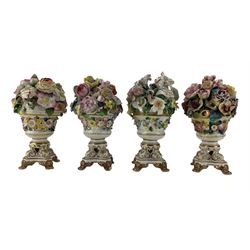 Four early 19th century Derby porcelain urns, each with a display of floral encrusted flowers, on gilt scroll base with four paw supports, H18cm max (4) Provenance: From the Estate of the late Dowager Lady St Oswald