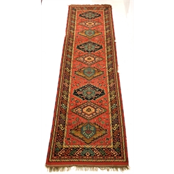 Red ground woollen runner rug, with lozenge and geometric design enclosed by multi line border, 340cm x 102cm