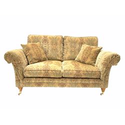 Parker Knoll - two seat sofa, upholstered in golden medallion fabric, with two small cushions and supported by two brass castors. W 180cm, height to seat 49cm