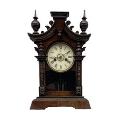  A German 19th century striking mantle clock in a wooden case on a canted plinth, curved top with carving and finials, 30hr Junghans movement striking the hours on a coiled gong, with a full-length glazed door, dial with Roman numerals, minute track and  Junghans logo, moon hands and winding collets, visible faux mercury pendulum.


