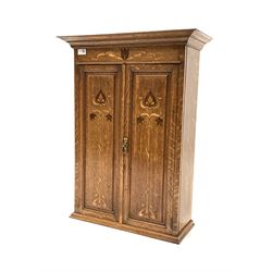 Early 20th century Art Nouveau oak wall hanging cupboard, projecting cornice over frieze and two fielded panelled doors with stylised floral inlay, enclosing two shelves W57cm, H76cm, D24cm
