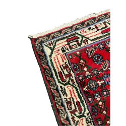 Persian crimson ground rug, the field with a central lozenge surrounded by stylised plant motifs, surrounded by a geometric ivory guard, with tendrils of green running throughout