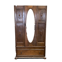 Early 20th century oak single wardrobe, with bevelled oval mirror enclosing interior fitted for hanging, one drawer under, raised on compressed bun supports