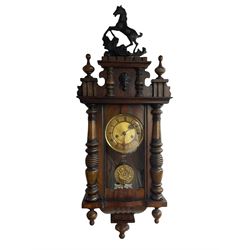 A German spring driven wall clock c1900 in a compact mahogany veneered Vienna style case, with a full-length glazed door and turned pillars attached, decorative pediment with a prancing horse and turned finials, two-part dial with a gilt centre, ivorine chapter ring with roman numerals, minute track and pierced gothic steel hands, with a repoussé gridiron pendulum and beat plate, eight-day movement striking the hours and half hours on a coiled gong.   With key. 



