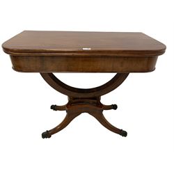 Regency mahogany tea table, rectangular fold-over and swivel top, raised on curved support with beaded collar and concave quadruform base decorated with applied roundells, on four sabre supports with brass paw feet and castors