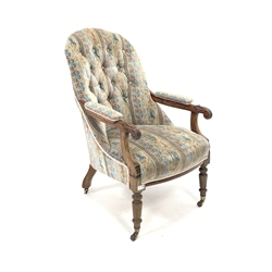 Late Victorian walnut framed open armchair, upholstered in buttoned fabric, floral scroll carved arm terminals, raised on turned supports with brass cup and ceramic castors, 