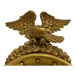 Regency gilt framed convex mirror, the eagle pediment with outstretched wings and turned head, surmounted on rocks, the circular plate with ebonised reeded slip within cavetto frame, applied with spherical mounts