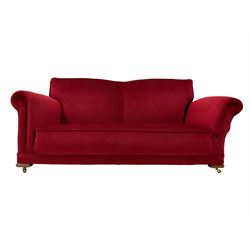 Early 20th century drop arm sofa, upholstered crimson fabric with sprung back and seat, raised on brass castors