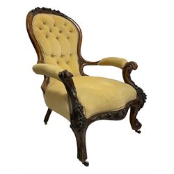 Victorian walnut open armchair, the arched cresting rail carved with flower heads with extending foliage, upholstered in pale yellow buttoned fabric, scroll carved arm terminals over serpentine supports and cabriole feet, carved with flower heads, foliage and berries, shaped lower rail carved with further decoration, the feet terminals carved with scrolled leaves, on brass castors 
