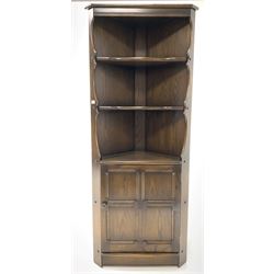 Ercol corner cabinet, two shaped edged shelves above single panelled cupboard enclosing interior, raised on stile supports (H184cm, W85cm, D42cm)
