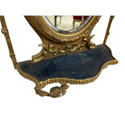 Victorian ornate gilt gesso framed mirror, pierced ribbon bow pediment with trailing foliate border atop the small bevelled mirror plate, acanthus leaf and foliate swags connect to the spear-topped uprights adorned with further foliate decoration, the main oval bevelled plate with a foliate and beaded frame connected to the smaller with a candle shelf, a larger serpentine shelf below the larger mirror plate with a trailing laurel leaf base with flowerheads