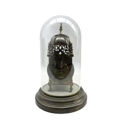 A small early 20th century replica Lantern clock with a French twin train striking movement and lever platform movement, striking the hours and half hours on a visible silvered bell, with a silvered chapter ring with Roman numerals and gothic steel hands, under an associated glass dome and 7” spun brass base.

