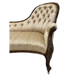Victorian mahogany framed chaise longue, curved moulded frame carved with scrolled foliage, upholstered in buttoned champagne fabric, on cabriole front feet with scrolled terminals, brass castors