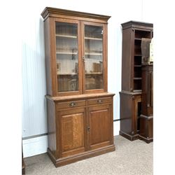 Edwardian oak bookcase on cupboard, two glazed doors enclosing three adjustable shelves, two drawers and two panelled cupboard doors under, bearing ivorine makers label reading 'Holiday, son & co. LTD. Birmingham' W107cm, H228cm, D50cm
