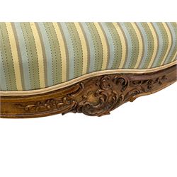 Late 20th century French walnut settee, the shaped cresting rail carved with foliate scroll cartouche and trailing foliage, upholstered back, arms and sprung serpentine seat in striped fabric, shaped apron carved with c-scroll cartouche, moulded cabriole supports
