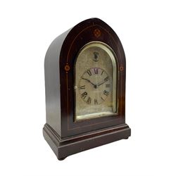 An Edwardian mahogany mantle clock with contrasting satinwood inlay c1905, in a lancet topped case on a projecting plinth with bun feet, silvered sheet dial with etched engraving, Roman numerals and minute track, subsidiary silent/chime dial and steel spade hands, with an arch topped glazed door and silvered slip, two train Westminster chiming movement, chiming on four gong rods, eight -day German movement manufactured by the Hamburg American Clock Company or HAC. HAC was formed in Germany in 1873 by Paul Landenberger . With pendulum.  



