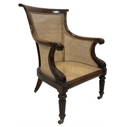 Victorian mahogany framed bergere armchair, the scrolled cresting rail and arms surrounding cane back and seat, raised on turned and reeded supports, terminating in brass castors  