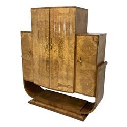 Attributed to Harry & Lou Epstein - Art Deco circa. 1930s figured walnut cocktail cabinet, enclosed by two scallop fluted doors, the maple and mirrored interior fitted with shelves, slide and cupboard, flanked by two side cupboard with internal drawers, curved supports on undertier with moulded base