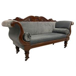 William IV mahogany two seat settee, scroll and foliate carved cresting rail, twin scrolled arms over moulded frieze rail, raised on turned supports with castors, upholstered in slate blue fabric with matching bolster cushions
