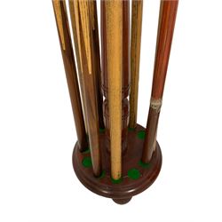Mahogany snooker cue stand, with cone finial on turned upright, fitted with twelve brass holders, circular base with resters on bun feet, together with five ash cues and four cue holders