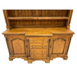 Traditional pine dresser, projecting cornice over pierced foliate frieze, the three-tier plate rack flanked by reeded pilasters, breakfront base fitted with four central drawers with arch panelled cupboards to either side, raised on bracket feet