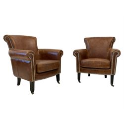 Pair traditional shaped armchairs, scrolled cresting rail and arms, upholstered in brown leather with studwork, on square supports with castors