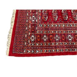 Persian Bokhara red ground rug, the field decorated with five columns of Gul motifs with surrounding geometric shapes, the symmetrical guarded border with repeating patterns in amber and ivory