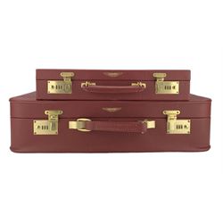 Late 20th century Aston Martin red leather suitcase and an attaché, by Tanner & Krolle, with brass combination locks and mounts, stamped with gilt Aston Martin emblem, the suitcase with red silk lined interior with two pockets, the attaché fitted with a folio, suitcase 59cm wide, attaché 42.5cm wide (2)