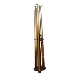 Mahogany snooker cue stand, with cone finial on turned upright, fitted with twelve brass holders, circular base with resters on bun feet, together with five ash cues and four cue holders