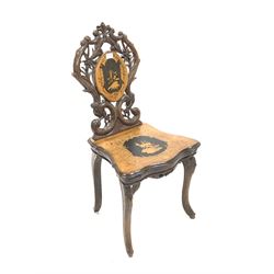 Late 19th century Swiss walnut music chair, the back rest carved with flower heads, plants and conforming scrolls centred by a penwork panel, the shaped seat with marquetry and penwork housing wind up cylindrical music box, raised on cabriole supports