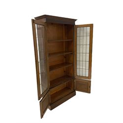 20th century oak bookcase, the projecting cornice and carved frieze over two leaded glazed doors opening to reveal three adjustable shelves, over cupboard, raised on a plinth base W90cm, H190cm, D37cm