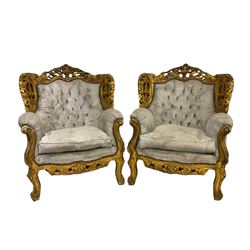 Pair Louis XVI design gilt wingback armchairs, the ornate cresting rail pierced and carved with scrolling foliate decoration and flower heads, the apron decorated with a central moulded and pierced cartouche, raised on cabriole supports, upholstered in buttoned pale blue damask fabric with sprung seat