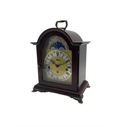 Compact late 20th century German Westminster chiming mantle clock in a break arch mahogany effect case with a brass carrying handle, conforming glazed door, etched brass dial with a silvered “Dutch” chapter ring, Roman numerals and minute track, steel serpentine hands with a working moon phase feature, Hermle 8-day three-train spring driven movement with a floating balance, chiming the quarters and hours on 5 gong rods.

