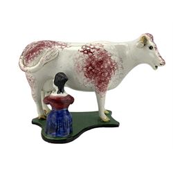 19th century cow creamer, probably Staffordshire, with curled tail handle, a milkmaid seated to one side with pail, decorated with sponged puce and set on concave green and black painted base, L20cm x H14cm