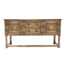 18th century style oak dresser base, with fitted drawer and another drawer flanked by two fielded cupboards, floral scroll carved apron, all raised by turned and block supports united by stretchers, 