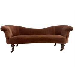 Late 19th century low-back settee, serpentine back and front, upholstered in velvet fabric with sprung seat and raised on turned feet with brass castors