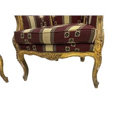 Pair Louis XV design gilt framed wingback armchairs, the cresting rail carved and moulded with a central cartouche and extending scrolling, the apron and knees decorated with flower heads, raised on cabriole supports, upholstered in maroon patterned fabric with sprung seat studwork