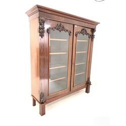 Late Victorian mahogany display cabinet bookcase, projecting cornice over two arched glazed doors with leaf carved corbels and applied floral moulding, enclosing four adjustable shelves, raised on square fluted supports, Formerly the top section of a bookcase on cupboard. W151cm, D47cm