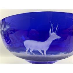 19th century Bohemian blue overlay glass bowl of pedestal form, engraved with a continuous scene of leaping deer in a woodland landscape, upon clear slice cut base, D23.5cm x H16cm, together with a pair of similar glass decanters, the bodies engraved with trailing grape and vine decoration, H37cm (3)