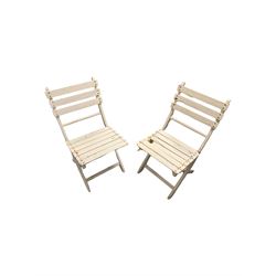Near pair of painted cast iron garden chairs with wooden slat back and seat, raised on scrolled supports, together with a folding wooden table and two matching chairs