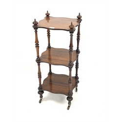 Small Victorian rosewood three tier whatnot, with turned finials, serpentine shelves, raised on turned supports and brass castors, 