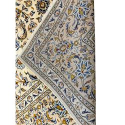 Persian Kashan ivory ground carpet, the field decorated with all-over palmettes interlaced with scrolling branches and foliage, the guarded border with floral patterns entwined with extending leafage and flower heads