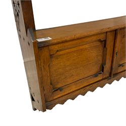 Late Victorian oak wall hanging shelf, shaped end supports pierced with stylised foliate motif, enclosed by two panelled doors