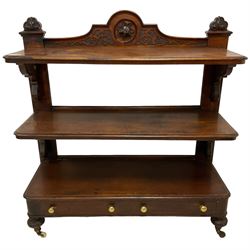 Victorian mahogany three-tier buffet, raised back with scrolling caved foliate decoration and central applied floral motif, scrolled and pierced brackets, fitted with two drawers to base, on egg and dart carved baluster supports with ceramic castors