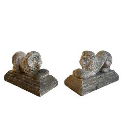 Pair of cast stone garden figures in the form of recumbent lions holding balls between their paws, raised on stepped moulded plinth bases, in crackled paint finish 