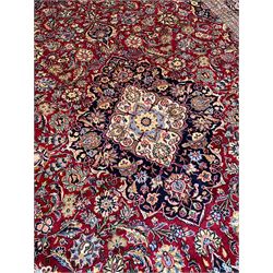 Persian Kashan red ground carpet, floral design shaped central medallion with scrolled borders, the field decorated profusely with scrolling foliage branches and stylised plant motifs, the repeating floral pattern border within guard bands